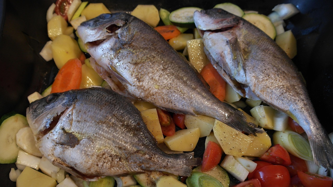 Pesce cotto in padella, dorato e perfettamente non attaccato, circondato da erbe aromatiche.