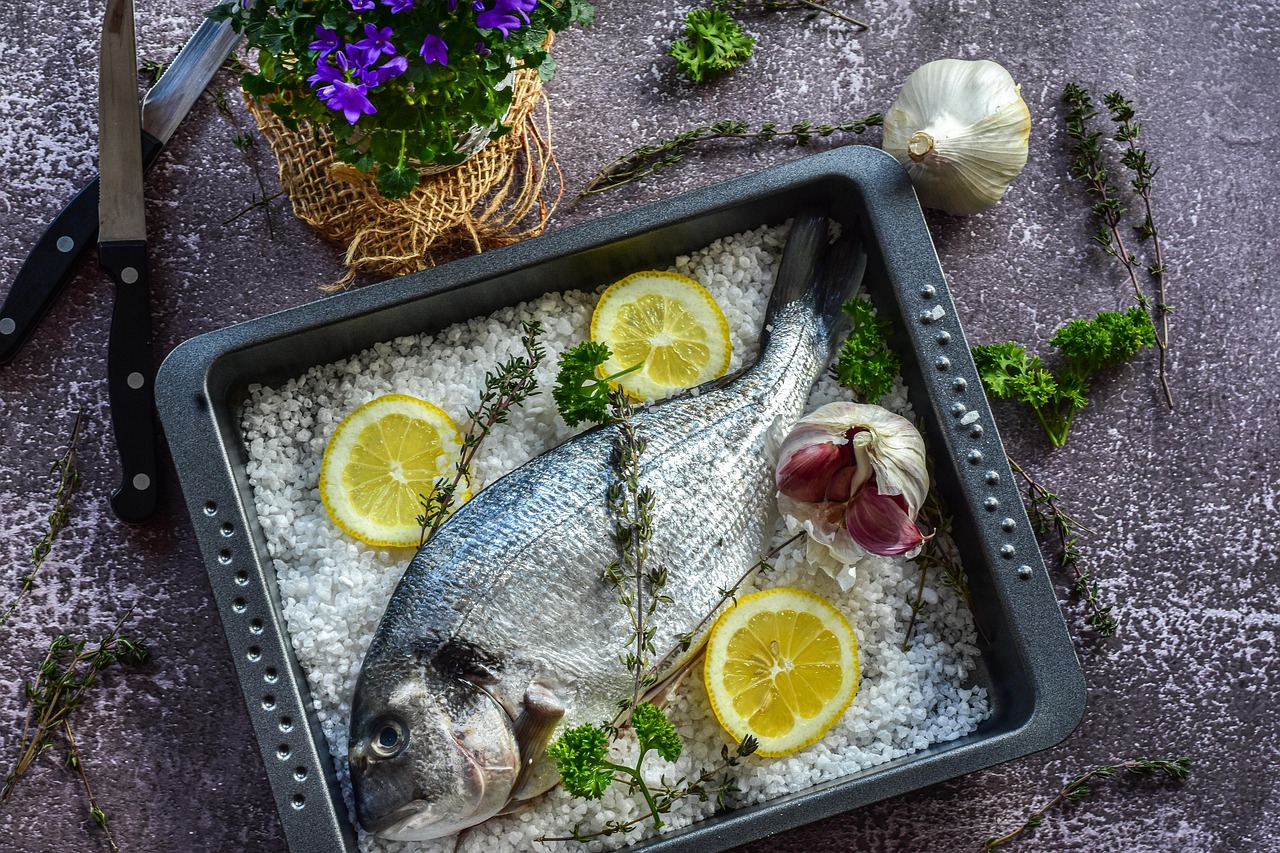 Filetti di pesce freschi su un tagliere, pronti per essere cucinati con erbe aromatiche e limone.